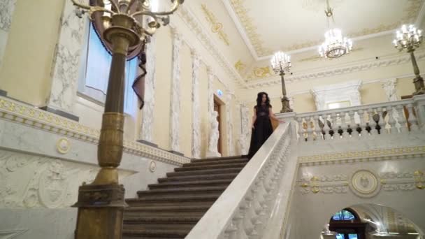 Mujer morena sexy joven en vestido de noche negro que baja en la escalera de piedra de mármol en palacio u hotel — Vídeos de Stock