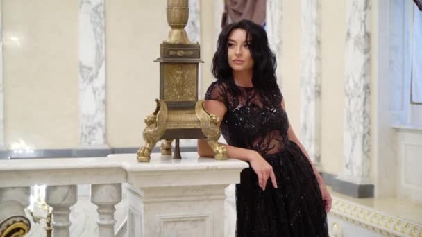 Ung sexig brunett kvinna i svart aftonklänning poserar på marmor sten stegen i palatset eller hotel — Stockvideo