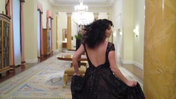 Joven mujer morena sexy en vestido de noche negro corriendo en palacio u hotel — Vídeos de Stock