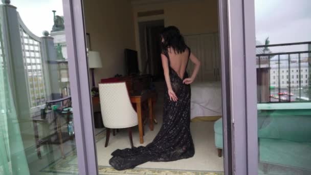 Young sexy brunette woman in black luxury dress staying in bedroom near window and undressing. — Stock Video