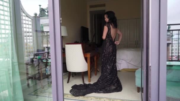 Jovem mulher morena sexy em vestido de luxo preto ficar no quarto perto da janela e despir . — Vídeo de Stock