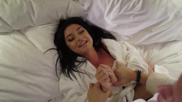 Young sexy couple at night laying in bedroom in white bathrobes and having fun. Smiling and laughting — Stock Video