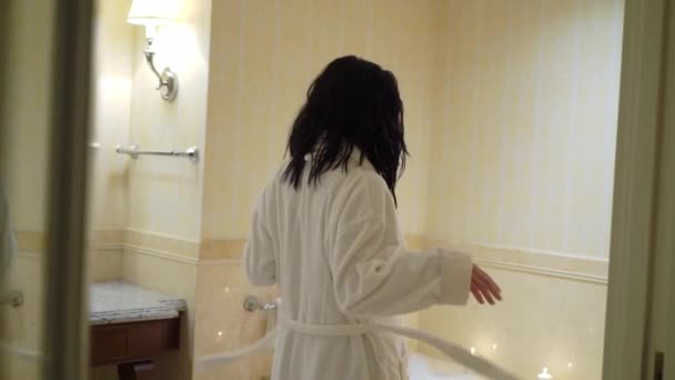 Молодая сексуальная брюнетка идет в ванную, раздевается снимая халат и лежа в ванне . — стоковое видео