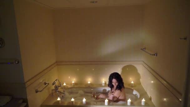 Junge sexy brünette Frau geht ins Badezimmer, zieht sich aus und legt sich in die Badewanne. — Stockvideo
