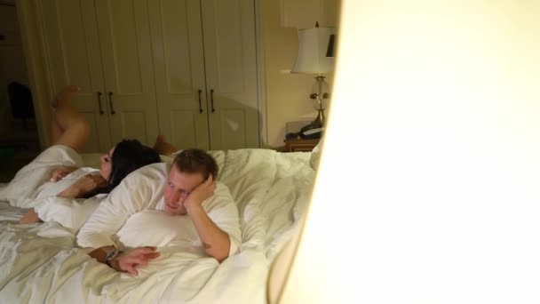 Jovem casal sexy à noite deitado no quarto em roupões de banho brancos ou toalha e abraço . — Vídeo de Stock