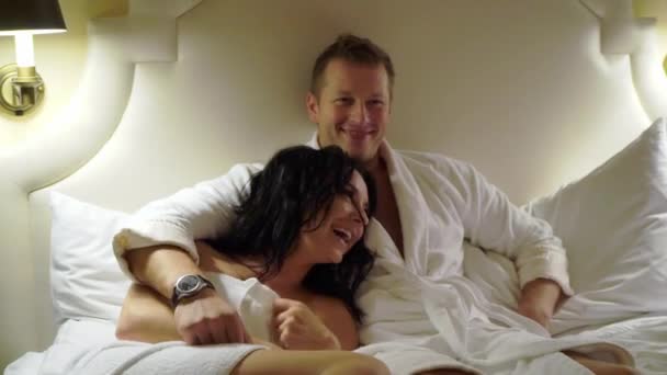Pasangan muda seksi di malam hari berbaring di kamar tidur di jubah mandi putih atau handuk dan memeluk . — Stok Video