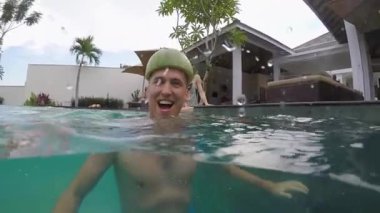 Genç bir adam bir kask karpuzun içinde partide havuzunda eğlenmek için. Tropikal bir villada tatil