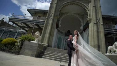 Genç gelin ve damat bir şehirde poz. Peçe rüzgarlı yaz gününde sallayarak.