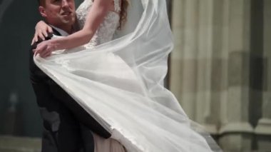 Genç gelin ve damat bir şehirde poz. Peçe rüzgarlı yaz gününde sallayarak.