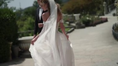 Genç gelin ve damat bir şehirde poz. Peçe rüzgarlı yaz gününde sallayarak.