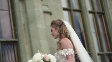 Genç gelin ve damat bir şehirde poz. Peçe rüzgarlı yaz gününde sallayarak.