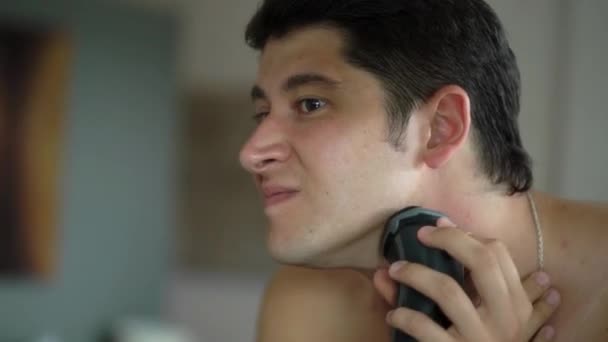 Guapo joven afeitándose con afeitadora eléctrica en el baño cerca del espejo — Vídeo de stock