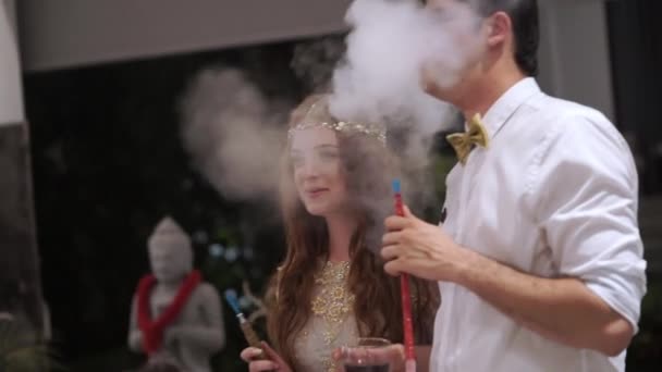 Άνδρας και γυναίκα στο κόμμα διασκεδάζουν και το κάπνισμα ναργιλέ. Γιορτάζοντας το γάμο, γενέθλια ή επέτειο. Εκδήλωση σε μια πολυτελή βίλα για τις διακοπές — Αρχείο Βίντεο