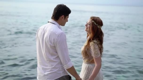 Newlyweds walking on the beach near sea at the evening or sunset. Holding hands, hugging. Romantic near ocean. — Stock Video