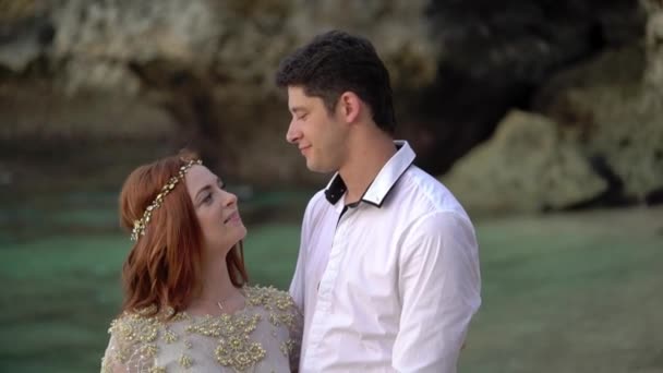 Newlyweds walking on the beach near sea at the evening or sunset. Holding hands, hugging. Romantic near ocean. — Stock Video