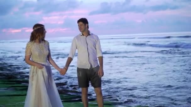 신혼 부부는 저녁 또는 일몰에 바다 근처 해변에서 산책. 손을 잡고, 포옹입니다. 로맨틱 한 바다 근처. — 비디오