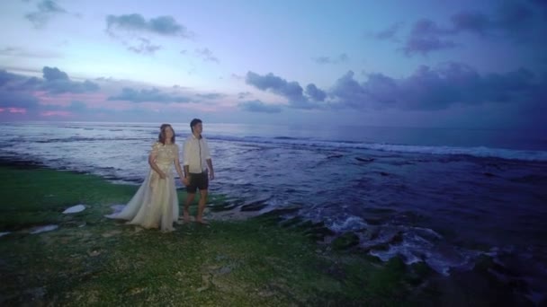 Recién casados caminando por la playa cerca del mar por la noche o al atardecer. Tomados de la mano, abrazados. Romántico cerca del océano . — Vídeo de stock