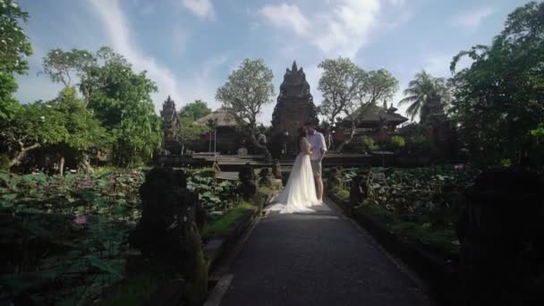 Newlyweds posing near buddhist temple in Bali. Holding hands, hugging. Romantic wedding. — Stock Video