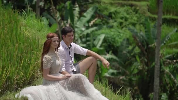 Newlyweds sitting and posing at rice terrace in Bali. Holding hands, hugging. Romantic wedding. — Stock Video