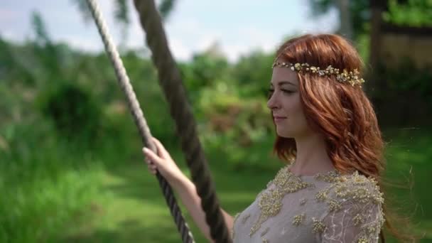 Een jonge vrouw op een schommel in Bali over een klif swingen. Roodharige bruid op haar trouwdag viering. — Stockvideo