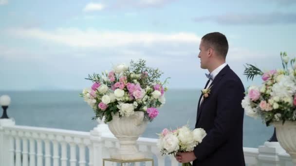 Молодой жених на свадебной церемонии стоит у алтаря арки и ждет невесту. Свадьба у моря — стоковое видео