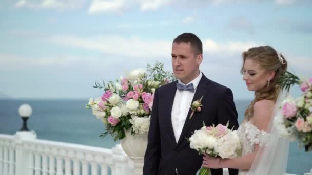 A menyasszony és a vőlegény az esküvői ceremóniát. Egy fiatal pár a szerelem az arch-on áll. Esküvő a tengerparton — Stock videók