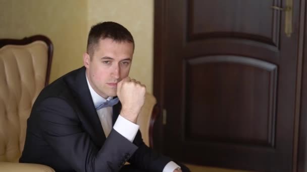 A young man in a black classic suit sitting on a chair and posing — Stock Video