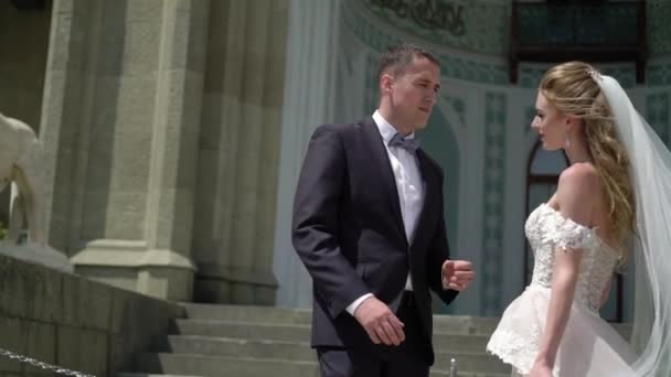 Unga bruden och brudgummen poserar i en stad. Viftande slöja på blåsig sommardag. — Stockvideo