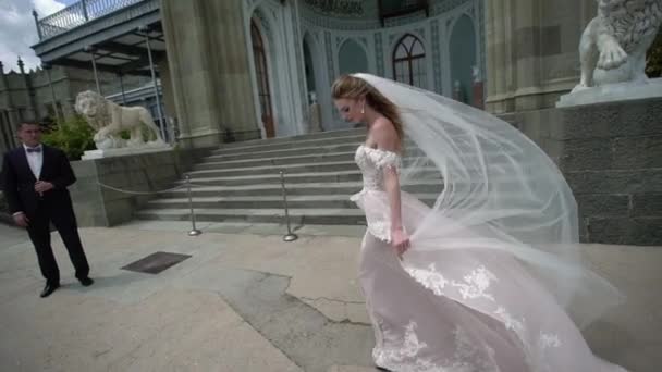 Fiatal menyasszony és a vőlegény pózol egy város. Fátyol integet szeles nyári nap. — Stock videók