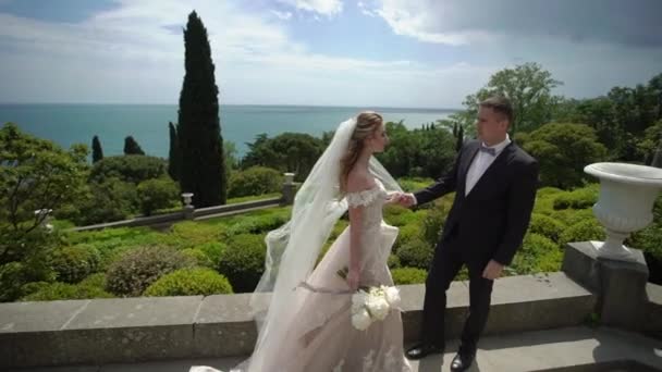 Молодая красивая невеста в свадебном платье и жених обнимает и целует — стоковое видео