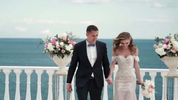 Los novios en la ceremonia de la boda. Una joven pareja enamorada pasando por invitados lanzando pétalos de rosa. Boda junto al mar — Vídeos de Stock