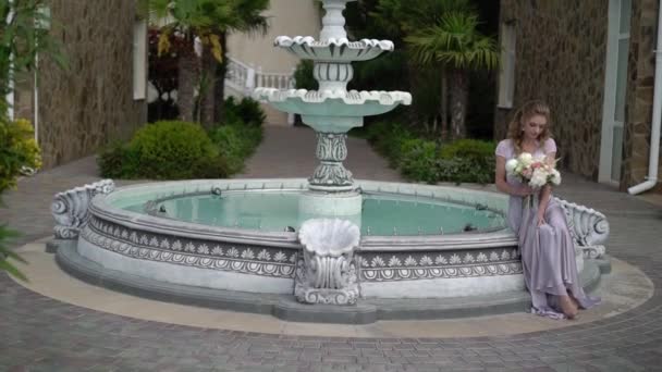 ランジェリーの噴水の近くの庭でブライダル ブーケとポーズで若いブロンドの女性 — ストック動画