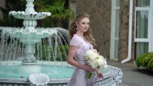 Ung blond kvinne i undertøy som poserer med brudebukett i hagen ved fontenen – stockvideo