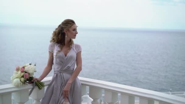 바다 전망 테라스에서 신부 부케와 포즈 란제리에서 젊은 금발 여자 — 비디오