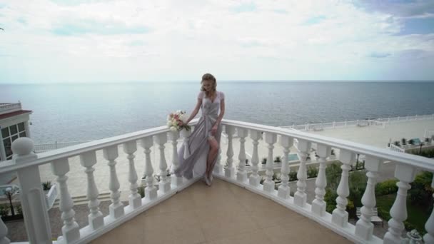 Jonge blonde vrouw in lingerie poseren met bruids boeket op terras met uitzicht op zee — Stockvideo