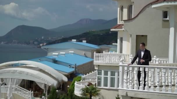 Mann im klassischen schwarzen Anzug auf dem Balkon am Meer. Geschäftsmann oder Bräutigam — Stockvideo