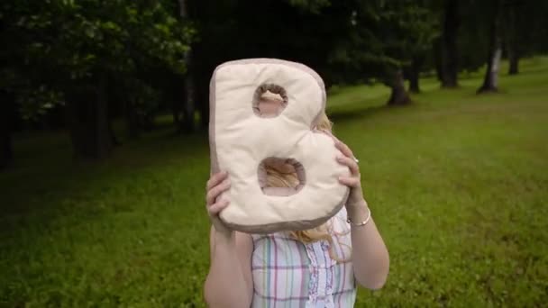 Joven chica encantadora divertirse en un parque en verano. Mujer posando con letra de almohada B — Vídeos de Stock