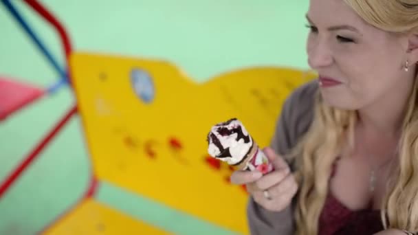 食べるとアイスクリームを舐めているスイングで若い素敵なブロンドの女の子 — ストック動画