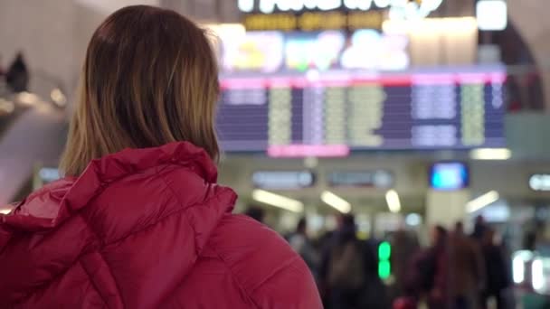 Bela jovem turista no aeroporto internacional ou estação ferroviária, perto de bordo de informações de voo — Vídeo de Stock