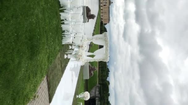 Κάθετη βίντεο. Γαμήλια τελετή διακοσμημένα σε εξωτερικούς χώρους κοντά σε λίμνη στο πάρκο κοντά στο παλάτι. Ηλιόλουστη καλοκαιρινή μέρα. Διακόσμηση με λευκά χρώματα και λουλούδια — Αρχείο Βίντεο
