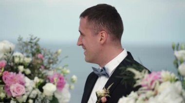 Genç damat düğün töreninde kemer sunak duruyor ve gelin için bekler. Denizin kenarında düğün
