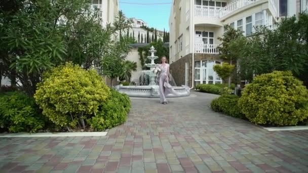 Молода блондинка в нижній білизні позує з весільним букетом в саду біля фонтану — стокове відео