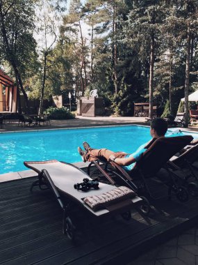 Genç esmer adam Yüzme Havuzu yakınındaki şezlong üzerinde dslr fotoğraf makinesi ve elektronik sabitleyici ile döşeme