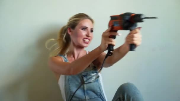 Молодая женщина в форме работает на стройке, играет с электрической дрелью, как пистолет — стоковое видео