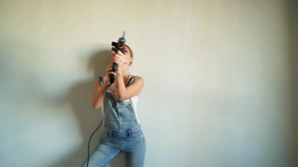 Mujer joven con uniforme trabajando en el sitio de construcción, jugando con taladro eléctrico como un arma — Vídeos de Stock