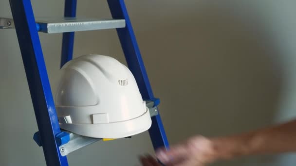 Casco blanco y escalera de metal azul en la obra de construcción de apariciones — Vídeo de stock