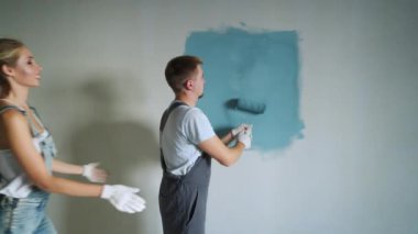 Genç aile çift işçinin silindir daire veya ev duvarlarda boya kullanarak.