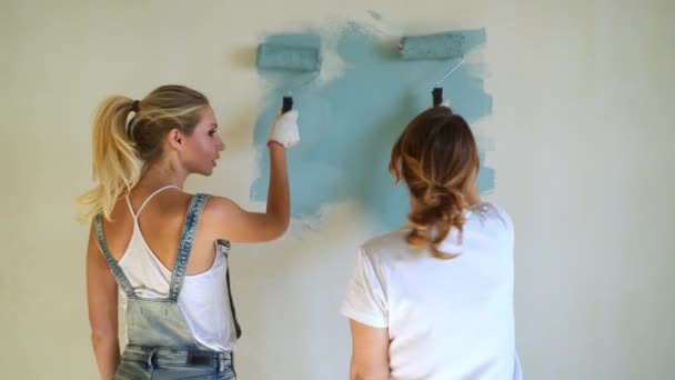 Две женщины, работающие на ролике, красят стены в квартире или доме. Строительство, ремонт и ремонт . — стоковое видео
