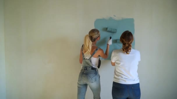 Две женщины, работающие на ролике, красят стены в квартире или доме. Строительство, ремонт и ремонт . — стоковое видео