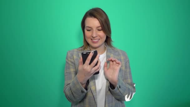 행복 한 예쁜 여 자가 고립 된 녹색 배경 위에 서 있는 동안 휴대 전화에 대 한 얘기 — 비디오